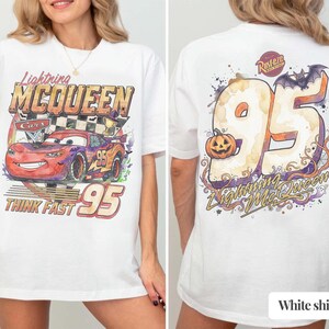 May include: A white t-shirt featuring a graphic of Lightning McQueen from Cars on the front with the text Lightning McQueen and Think Fast 95. The back displays a large number 95 with a pumpkin, a bat, and the text Rust-eze and Lightning McQueen.