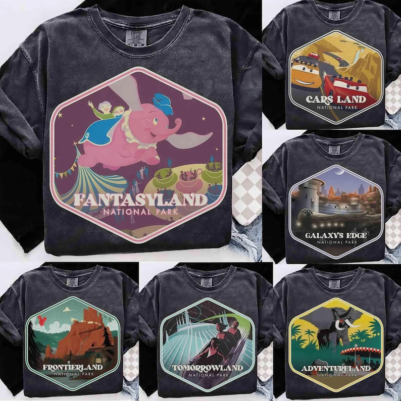 Op de afbeelding: Een antracietgrijs T-shirt met ronde hals en een grote zeshoekige print op de borst. De afbeelding toont een roze olifant die over een park vliegt met de tekst FANTASYLAND NATIONAL PARK. Andere T-shirts tonen ontwerpen voor Cars Land, Galaxy's Edge, Frontierland, Tomorrowland en Adventureland.