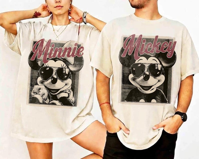 May include: Off-white t-shirts featuring a black and white image of Mickey and Minnie Mouse wearing sunglasses. The word "Minnie" is printed above Minnie's image in a maroon script, and "Mickey" is printed above Mickey's image.