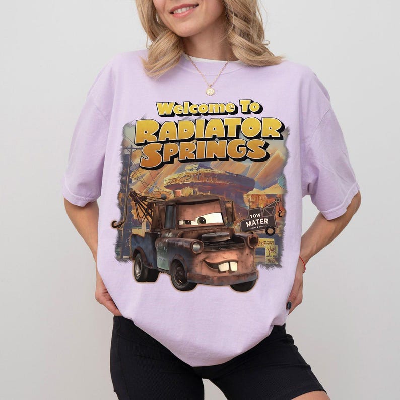 Pu&ograve; includere: T-shirt lilla chiaro con grafica del film Cars. La grafica dice "Welcome to Radiator Springs" e mostra il personaggio di Cricchetto. La maglietta &egrave; in stile casual.