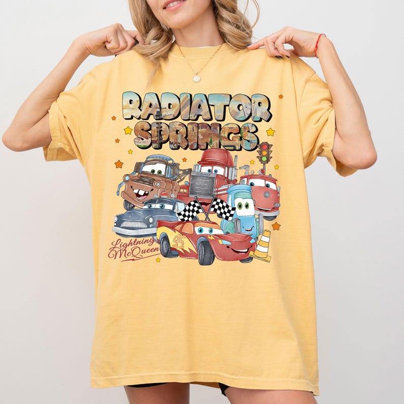 May include: Yellow t-shirt featuring a graphic of characters from the movie Cars, including Lightning McQueen, Mater, and others, with the text "Radiator Springs" and "Lightning McQueen". The design includes stars and a traffic light.