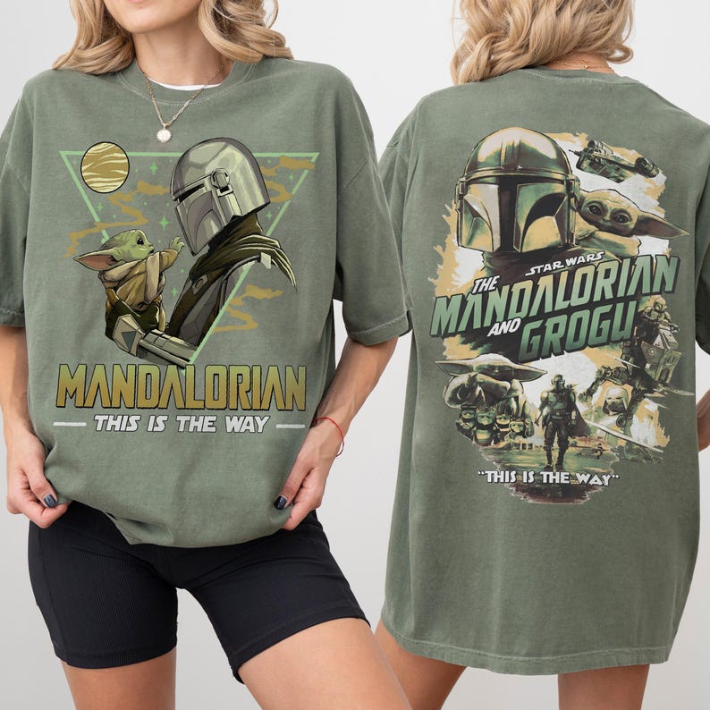 K&ouml;nnte beinhalten: Olivgr&uuml;nes T-Shirt mit einer Grafik von The Mandalorian und Grogu. Das Frontdesign enth&auml;lt den Text "MANDALORIAN" und "THIS IS THE WAY". Die R&uuml;ckseite des Shirts zeigt "THE MANDALORIAN AND GROGU" mit zus&auml;tzlichen Bildern.