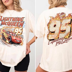 Puede incluir: Camiseta color crema con un gr&aacute;fico de Lightning McQueen. La parte delantera muestra el personaje con el texto "Lightning McQueen" y "95". La parte trasera de la camiseta muestra un gran "95" con llamas y el texto "Lightning McQueen".