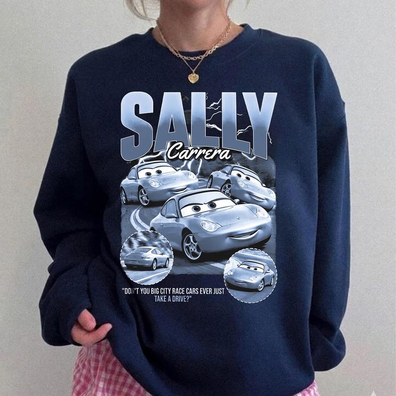 Puede incluir: Sudadera azul marino con un dise&ntilde;o de Sally Carrera de la pel&iacute;cula Cars. El dise&ntilde;o incluye el texto "SALLY Carrera" y la cita "DON'T YOU BIG CITY RACE CARS EVER JUST TAKE A DRIVE?"