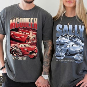 Puede incluir: Dos camisetas grises con gr&aacute;ficos de la pel&iacute;cula "Cars". Una camiseta muestra "Lightning McQueen" con coches de carreras rojos y la frase "KA-CHOW!". La otra camiseta muestra "Sally Carrera" con coches azules.