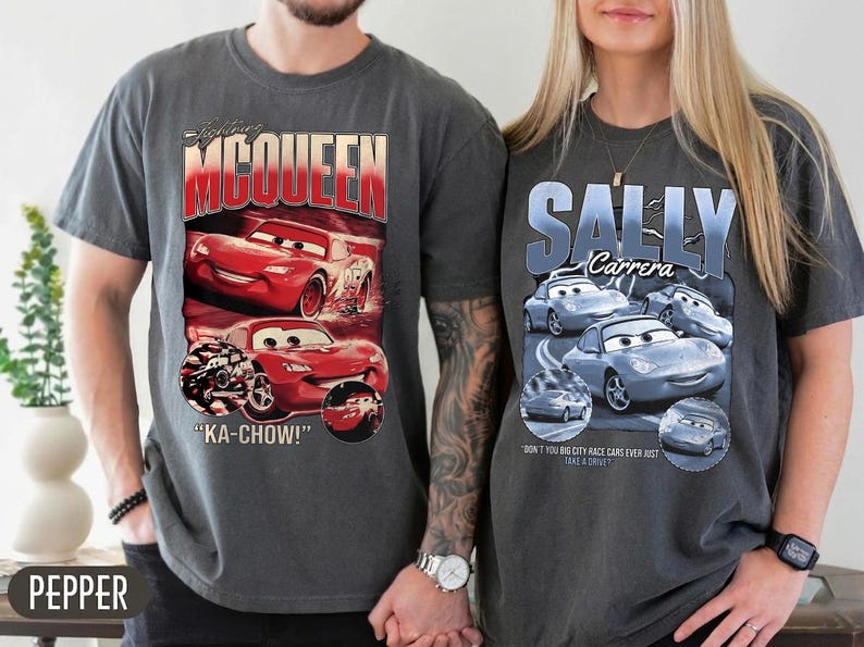 Puede incluir: Dos camisetas grises con gr&aacute;ficos de la pel&iacute;cula "Cars". Una camiseta muestra "Lightning McQueen" con coches de carreras rojos y la frase "KA-CHOW!". La otra camiseta muestra "Sally Carrera" con coches azules.