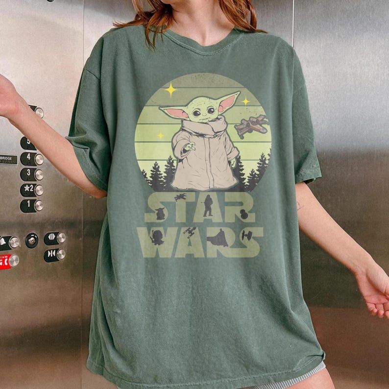 Op de afbeelding: Groen t-shirt met een afbeelding van Grogu uit Star Wars. Het ontwerp bevat Grogu, een ruimteschip en de tekst "STAR WARS". Het shirt heeft korte mouwen en een relaxte pasvorm.
