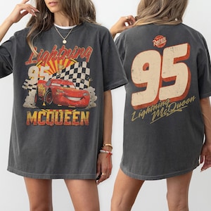 May include: Dark gray Lightning McQueen t-shirt featuring a graphic of the race car with the number 95, a checkered flag, and the text "Lightning McQueen" and "McQueen". The back of the shirt displays the number 95 and "Lightning McQueen".
