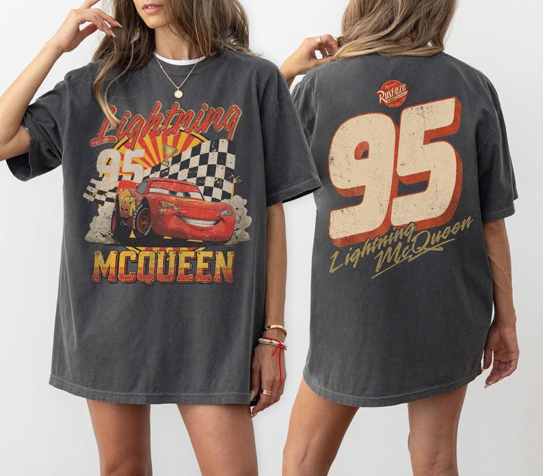 May include: Dark gray Lightning McQueen t-shirt featuring a graphic of the race car with the number 95, a checkered flag, and the text "Lightning McQueen" and "McQueen". The back of the shirt displays the number 95 and "Lightning McQueen".