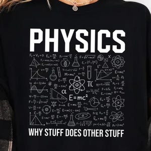 May include: Black t-shirt with the word "PHYSICS" in large white letters. Below the word are various physics formulas and diagrams. The phrase "WHY STUFF DOES OTHER STUFF" is printed below the formulas.