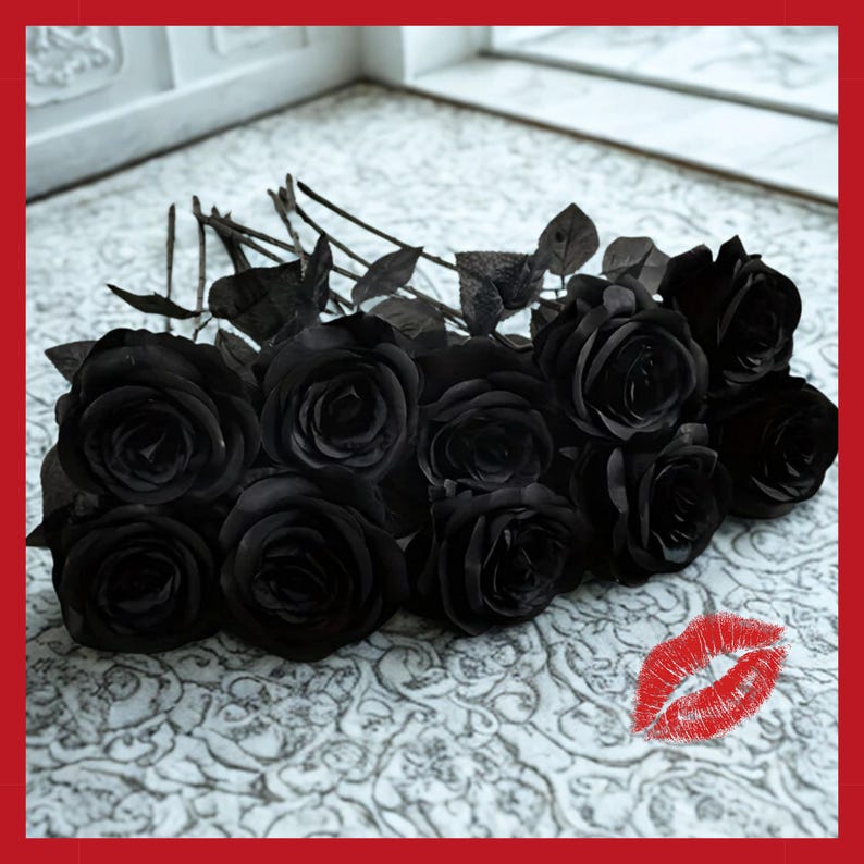 May include: A bouquet of black roses with dark green leaves. The roses are arranged on a white patterned surface. A red lipstick kiss mark is in the lower right corner. The roses are a dark, solid black color.