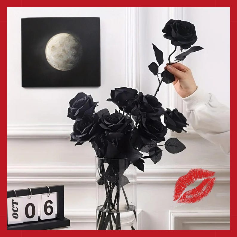 May include: A bouquet of black roses in a clear glass vase, with a single rose being held. A painting of the moon hangs on the wall. A black calendar displays the date, October 6th. A red lip print is on the wall.