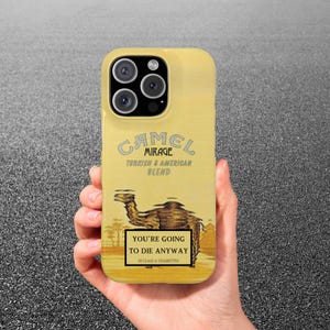 May include: A yellow phone case featuring a Camel Mirage design. The case includes the text "CAMEL MIRAGE TURKISH & AMERICAN BLEND" and "YOU'RE GOING TO DIE ANYWAY 20 CLASS A CIGARETTES". The case has a camel illustration.