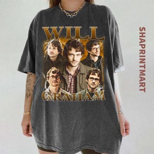 Puede incluir: Camiseta gris oscuro con un collage de imágenes de un hombre, con las palabras "WILL GRAHAM" en una fuente dorada de estilo vintage. La camiseta tiene un aspecto desgastado y vintage.