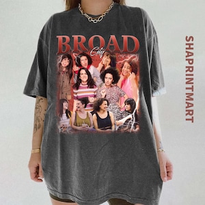Könnte beinhalten: Dunkelgraues T-Shirt mit einer Gruppe von Frauen und dem Text "BROAD City" in Rot. Das Shirt hat einen Vintage-Look. Der Markenname "SHAPRINTMART" ist vertikal auf der rechten Seite aufgedruckt.
