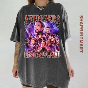 Może przedstawiać: Ciemnoszara koszulka z plakatem filmowym Avengers: Endgame. Projekt zawiera obrazy kilku postaci ze słowami "Avengers" i "Endgame" w czerwonych literach. Koszulka ma wygląd vintage.