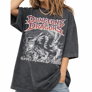 Könnte beinhalten: Dunkelgraues T-Shirt mit dem Text "DUNGEONS & DRAGONS" in Rot und Weiß sowie einer Grafik eines Drachen und Figuren. Das Shirt hat auch den Text "Never Split the Party".