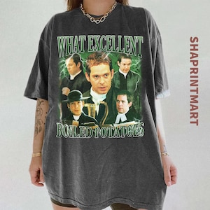 Puede incluir: Camiseta gris oscuro con un diseño gráfico verde y blanco. El diseño presenta el texto "WHAT EXCELLENT BOILED POTATOES" e imágenes de hombres. La camiseta tiene un aspecto vintage.