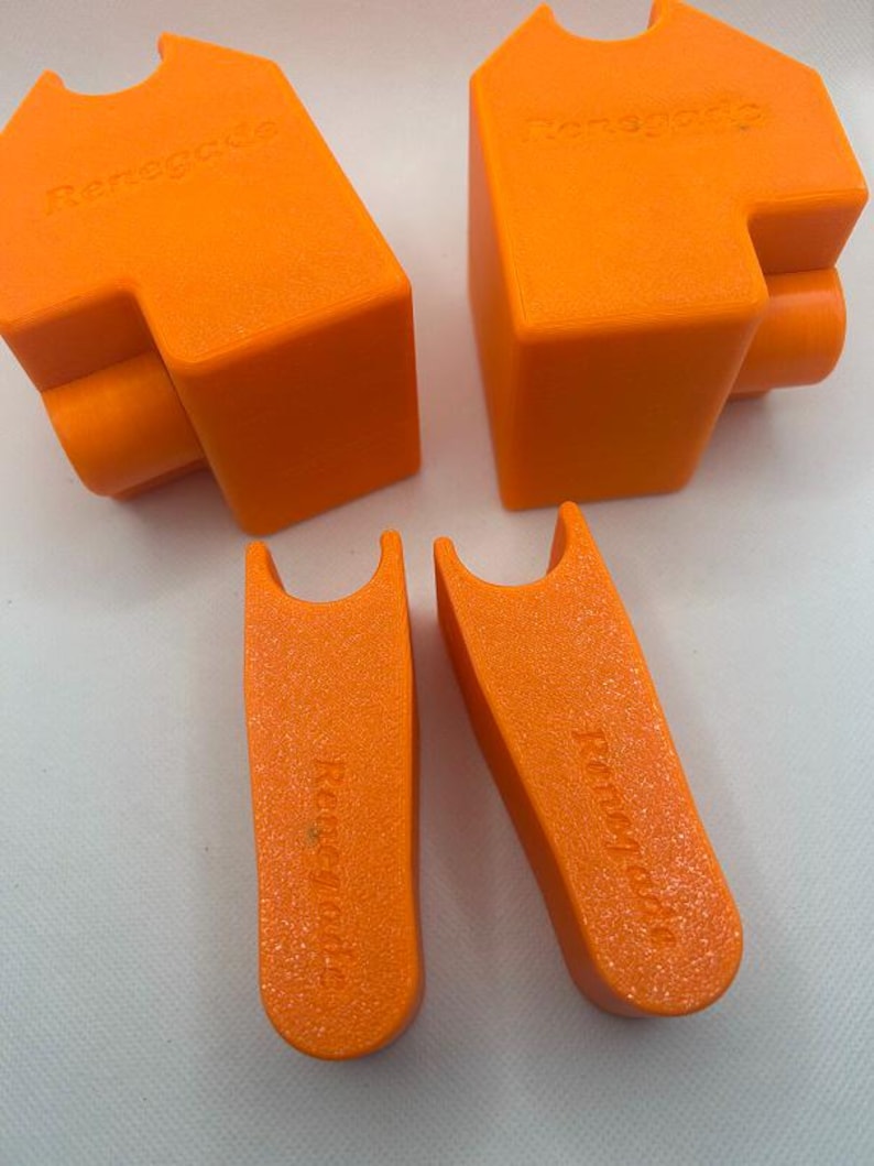 May include: Four bright orange 3D-printed objects are displayed against a white background. Two larger, angular pieces with the word "Renegade" are visible, along with two smaller, curved pieces also bearing the "Renegade" text. The objects have a matte finish.