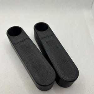 May include: Two black, rectangular objects with a cylindrical opening at the top. The word "Renegade" is printed on the side of each object. The objects have a textured surface and are placed side by side.