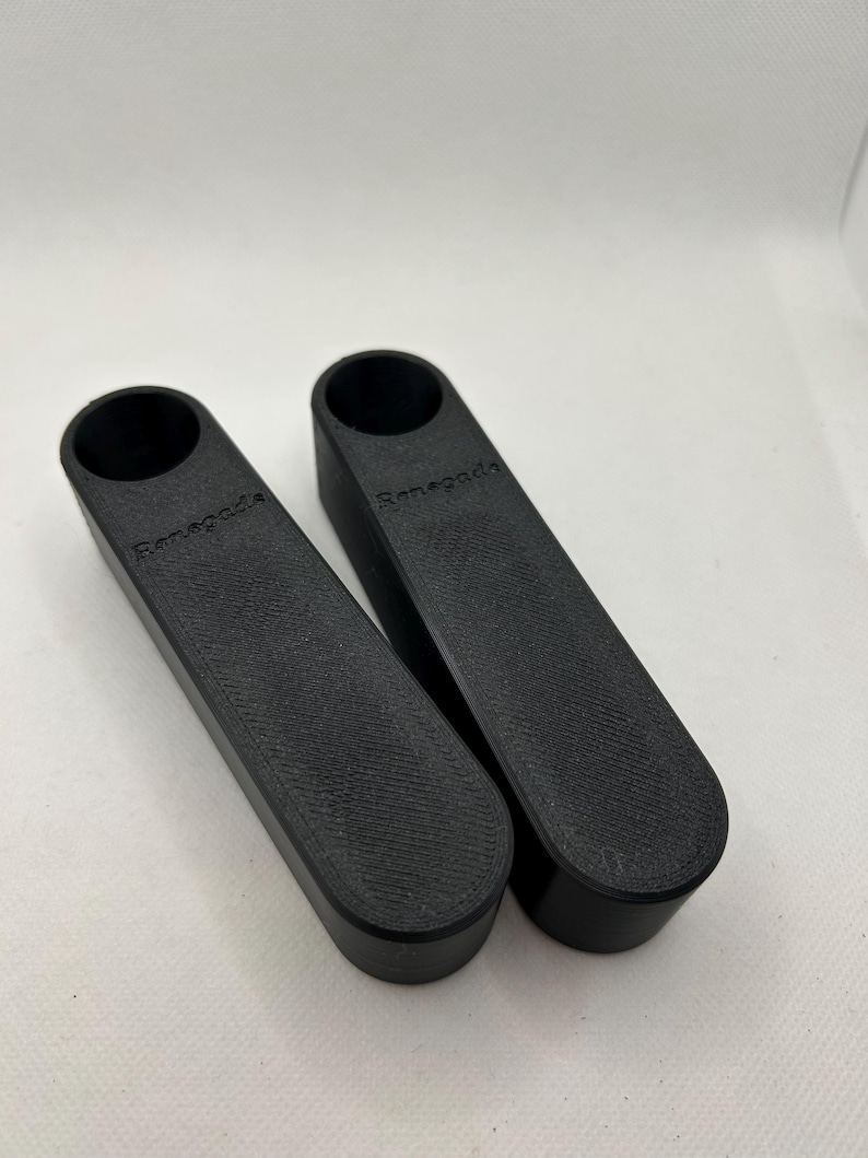 May include: Two black, rectangular objects with a cylindrical opening at the top. The word "Renegade" is printed on the side of each object. The objects have a textured surface and are placed side by side.