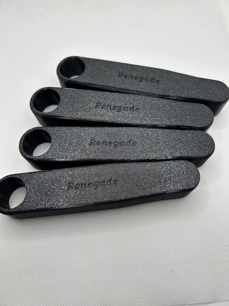 Pu&ograve; includere: Quattro oggetti rettangolari neri e strutturati con un foro arrotondato su un'estremit&agrave;. La parola "Renegade" &egrave; stampata su ogni oggetto. Gli oggetti sono disposti in modo leggermente sovrapposto su uno sfondo bianco.