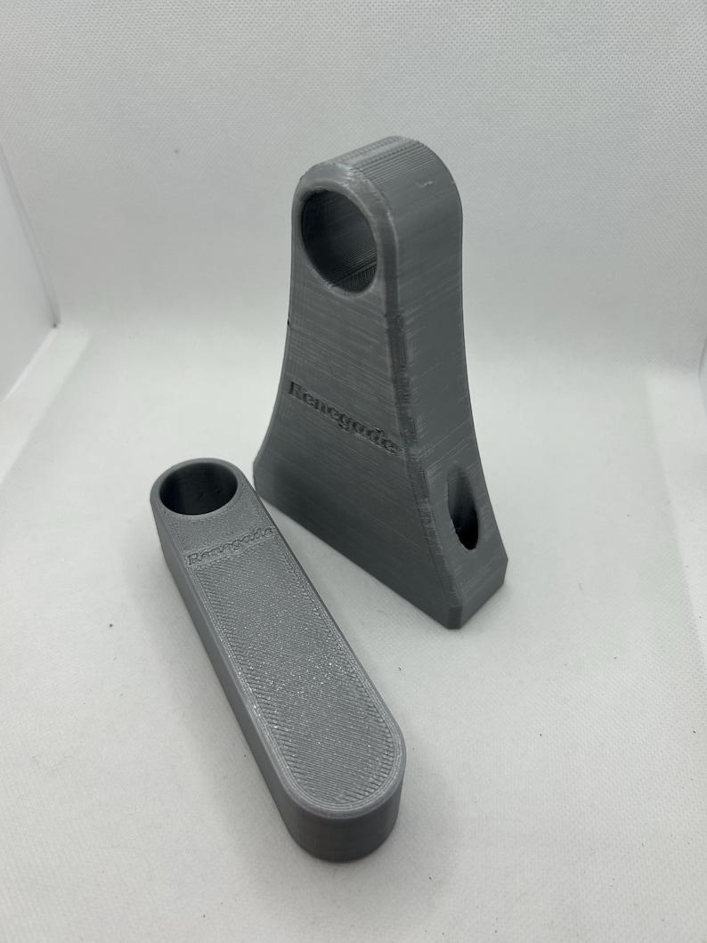 May include: Two gray 3D-printed objects. One is a tall, angled piece with a circular hole at the top and a smaller hole near the bottom. The other is a rectangular piece with a circular hole. Both pieces have the word "Renegade" printed on them.