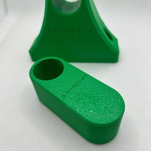 May include: Two bright green 3D-printed objects. One is a wedge-shaped stand with a circular opening and the word "Renegade" embossed on the side. The other is a smaller, rectangular piece with a similar texture and the word "Renegade" on its side.
