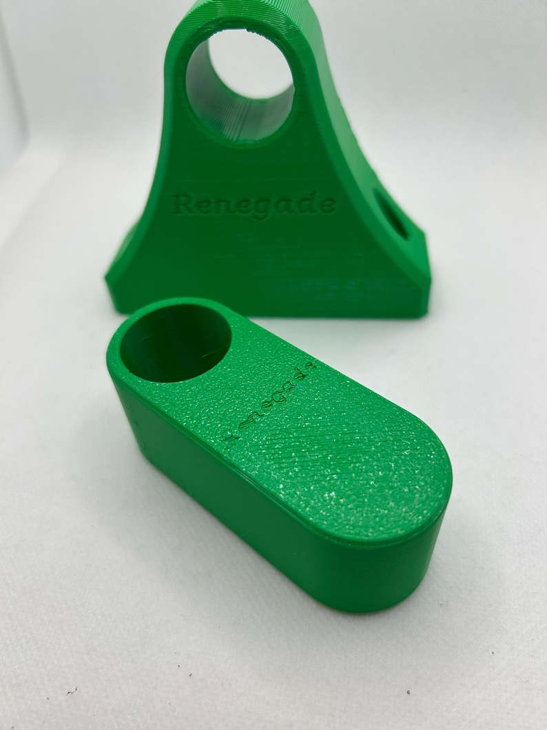 May include: Two bright green 3D-printed objects. One is a wedge-shaped stand with a circular opening and the word "Renegade" embossed on the side. The other is a smaller, rectangular piece with a similar texture and the word "Renegade" on its side.