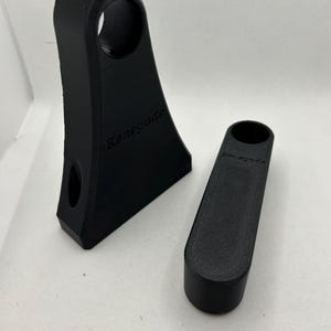 May include: Two black 3D-printed objects. One is a tall, angled piece with a circular hole and the word "Renegade" printed on it. The other is a smaller, cylindrical piece, also with "Renegade" printed on it.