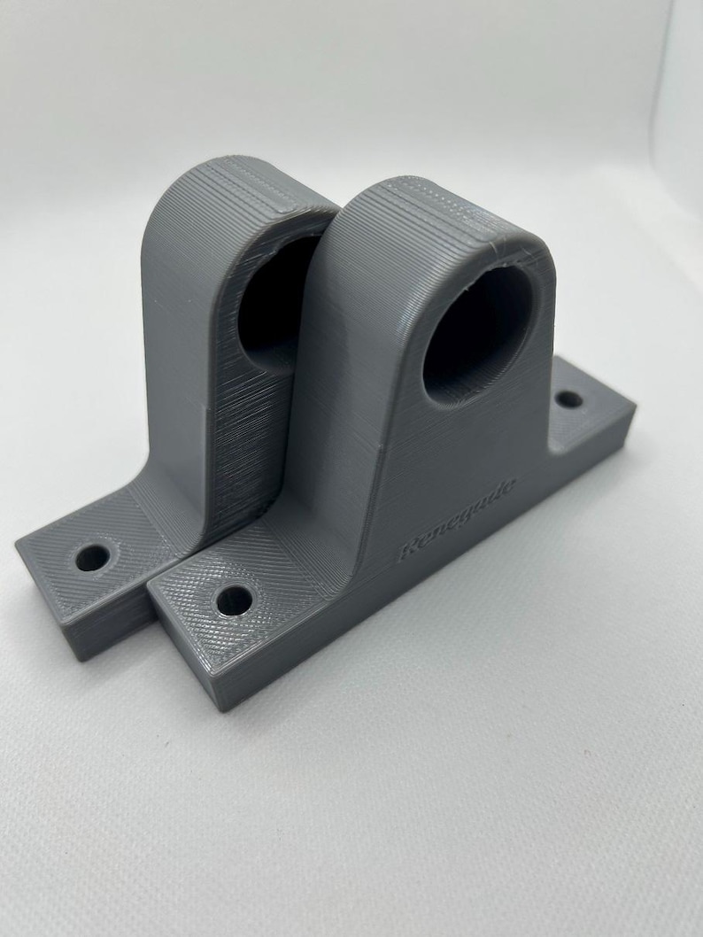 Puede incluir: Dos soportes grises impresos en 3D. Cada soporte tiene una parte superior curva con una abertura circular y una base rectangular con dos agujeros para el montaje. La palabra "Renegade" est&aacute; impresa en el lateral de un soporte.
