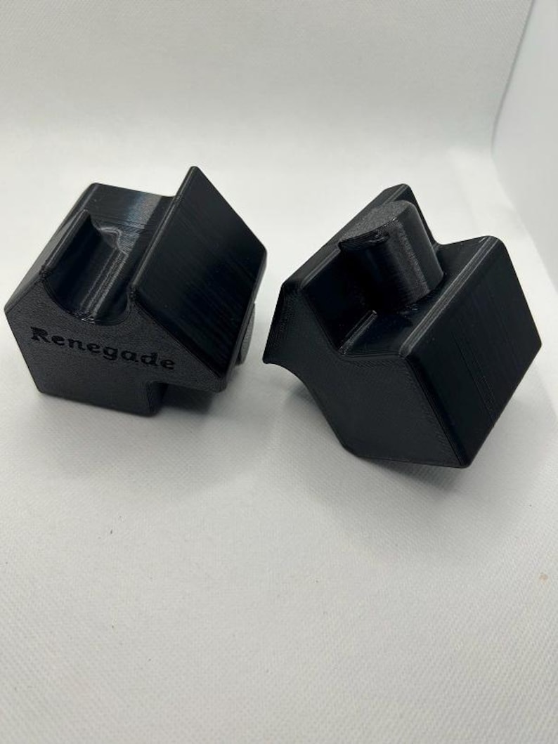 May include: Two black, geometric, 3D-printed objects. Each has a unique shape with angled surfaces and a central, raised cylindrical feature. The word "Renegade" is printed on one of the objects. The objects are displayed on a white surface.