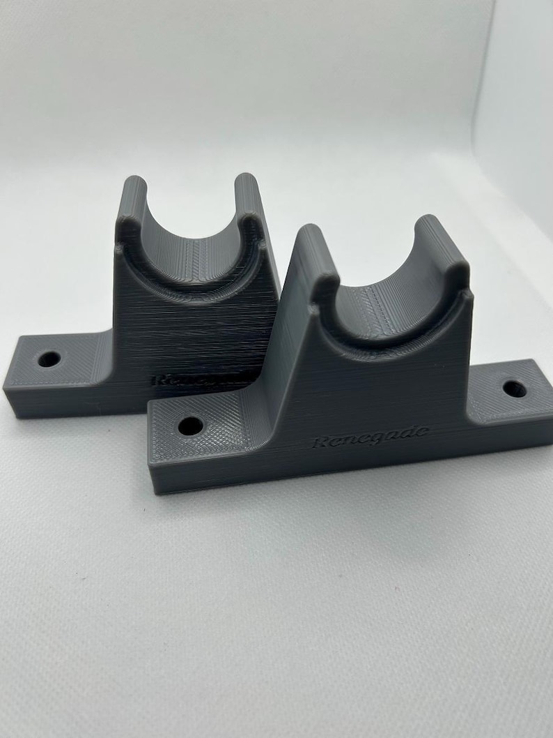 Puede incluir: Dos soportes grises impresos en 3D con un dise&ntilde;o de cuna curvada y una base plana con un agujero para el montaje. La palabra "Renegade" est&aacute; impresa en un soporte.