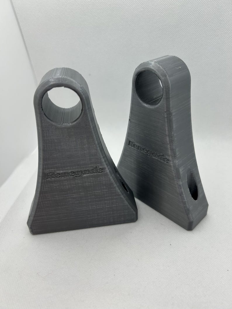 May include: Two gray 3D-printed brackets with a flared base and a circular opening at the top. The word "Renegade" is printed on the front of each bracket. The brackets are made of a textured material.