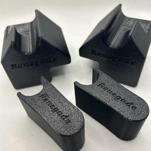 May include: Four black 3D-printed objects. Two are angled with a slot, and the other two are rectangular with a curved top. All pieces have the word "Renegade" printed on them. The objects are on a white surface.