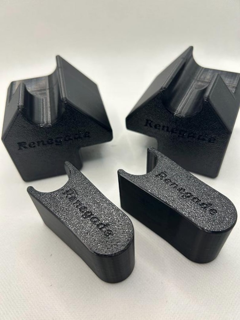 May include: Four black 3D-printed objects. Two are angled with a slot, and the other two are rectangular with a curved top. All pieces have the word "Renegade" printed on them. The objects are on a white surface.