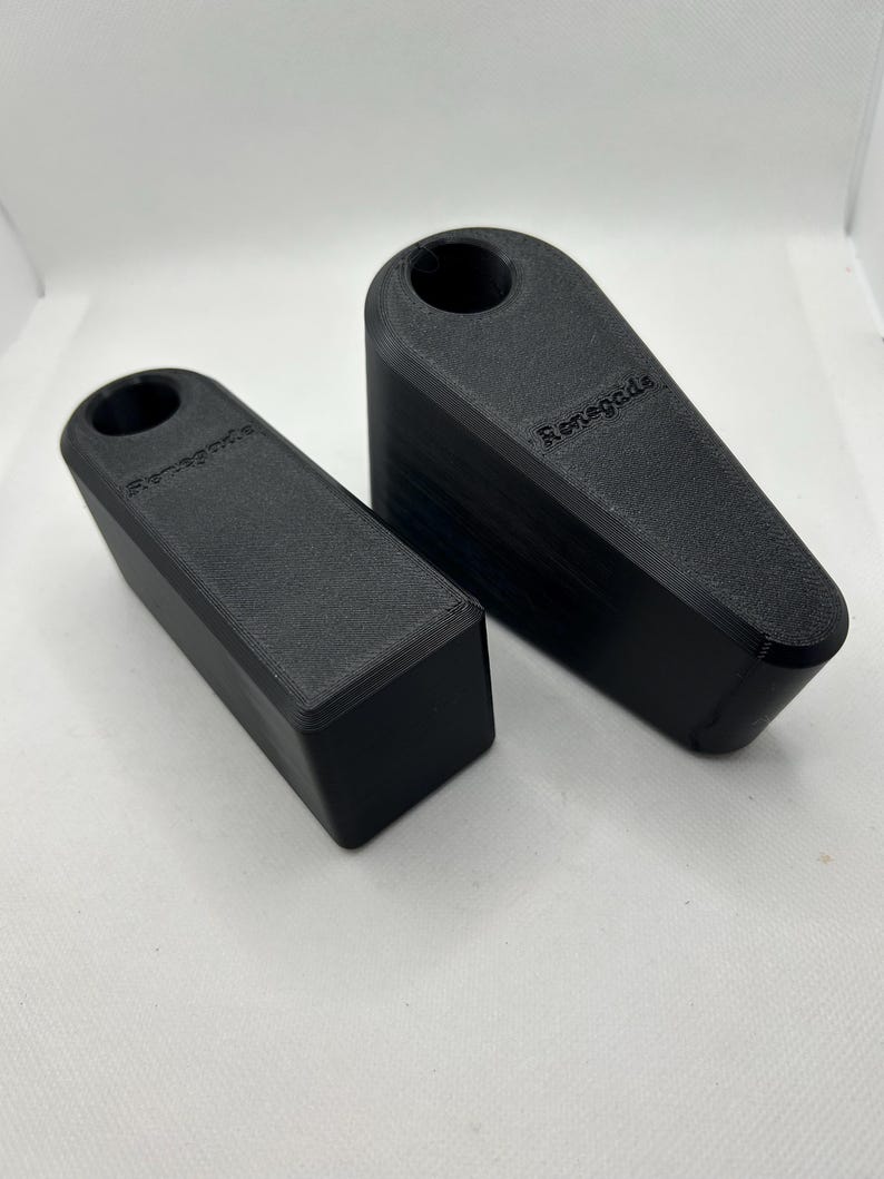 Puede incluir: Dos topes de puerta negros, uno m&aacute;s peque&ntilde;o y rectangular, el otro m&aacute;s grande e inclinado. Cada uno tiene la palabra "Renegade" impresa. Los topes de puerta est&aacute;n hechos de un material negro mate. El m&aacute;s grande mide unos 15 cm.