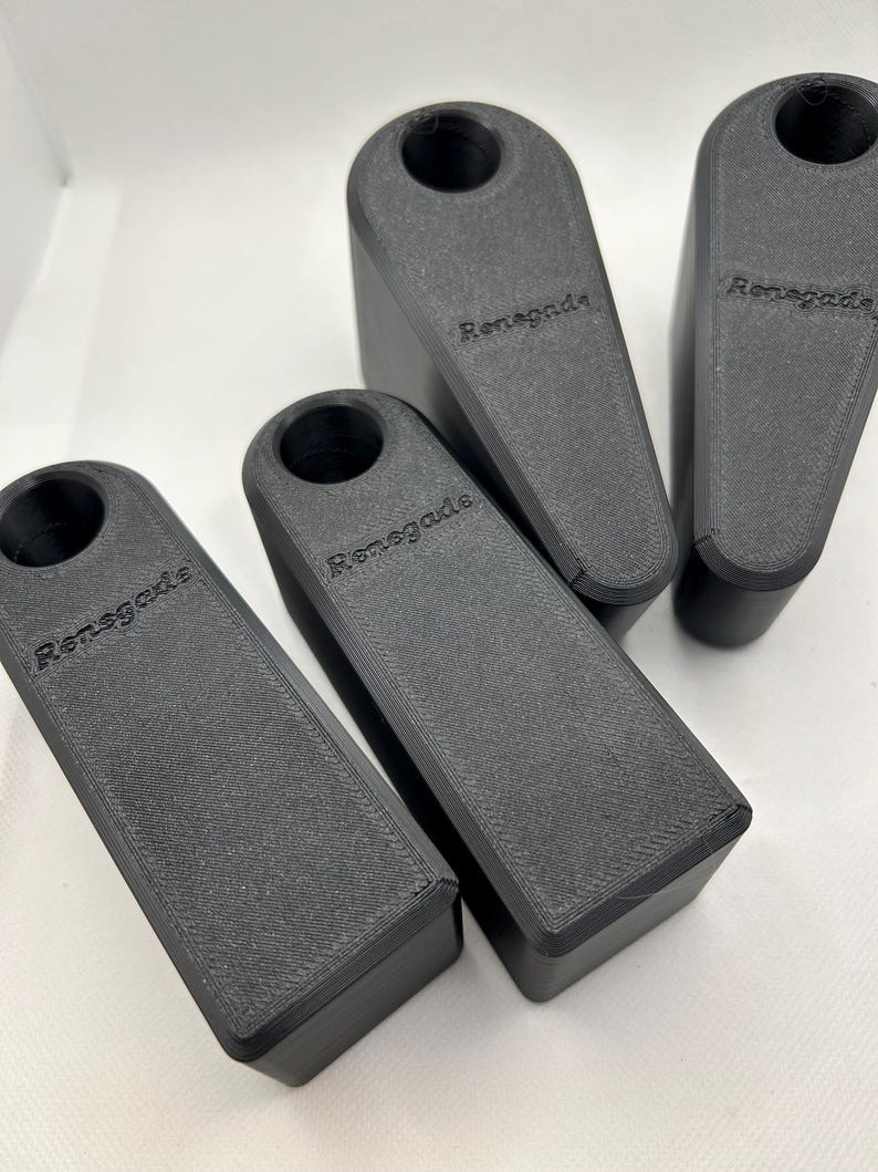 Puede incluir: Cuatro topes de puerta negros, rectangulares, con una parte superior redondeada. La palabra "Renegade" est&aacute; impresa en el lateral de cada uno. Est&aacute;n dispuestos sobre una superficie blanca.