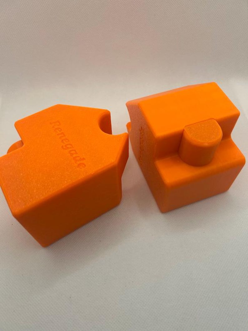 May include: Two bright orange, geometric blocks with the word "Renegade" embossed on one. The blocks have a textured surface and are designed to fit together. The background is a plain white.