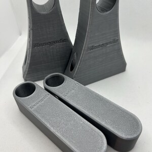 May include: Four gray 3D-printed objects. Two are tall with a circular opening at the top and the word "Renegade" on the side. The other two are rectangular with a circular opening and the word "Renegade" on the side. The objects have a textured surface.