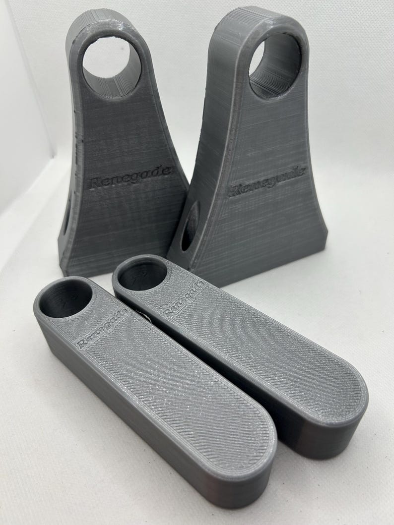 May include: Four gray 3D-printed objects. Two are tall with a circular opening at the top and the word "Renegade" on the side. The other two are rectangular with a circular opening and the word "Renegade" on the side. The objects have a textured surface.