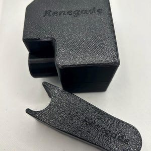 May include: Black textured plastic holder and tool. The holder has a rectangular shape with a curved top and the word "Renegade" embossed on the front. The tool is a flat, curved shape with the word "Renegade" embossed on it.