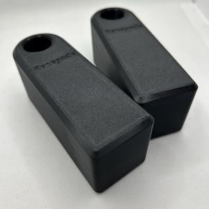 Puede incluir: Dos topes de puerta rectangulares negros con un agujero cil&iacute;ndrico en un extremo. La palabra "Renegade" est&aacute; impresa en el lateral de cada tope de puerta. Los topes de puerta est&aacute;n hechos de un material texturizado.
