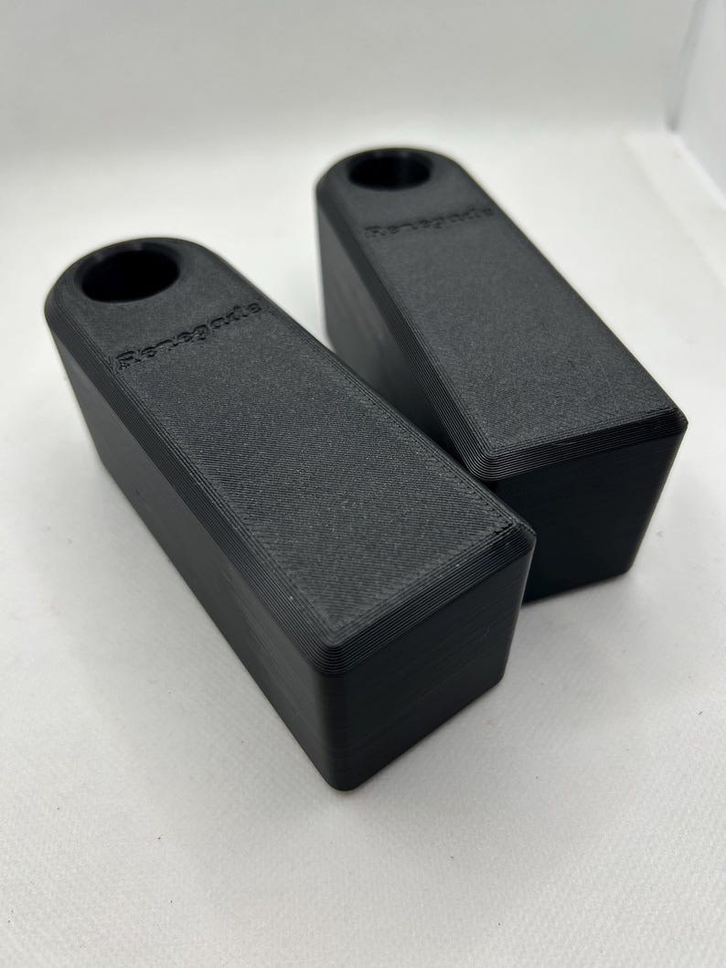 Puede incluir: Dos topes de puerta rectangulares negros con un agujero cil&iacute;ndrico en un extremo. La palabra "Renegade" est&aacute; impresa en el lateral de cada tope de puerta. Los topes de puerta est&aacute;n hechos de un material texturizado.