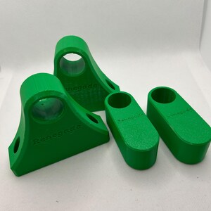 May include: Four bright green 3D-printed objects. Two are angled with a circular opening and the word "Renegade" printed on the side. The other two are rectangular with rounded ends and the word "Renegade" printed on the side.