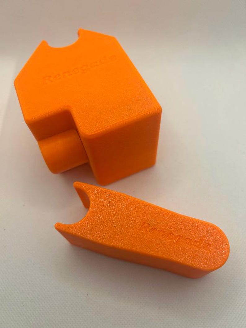 May include: Two bright orange, 3D-printed objects. One is a rectangular shape with a curved cutout and the word "Renegade" embossed on it. The other is a T-shaped piece with the word "Renegade" embossed on it.