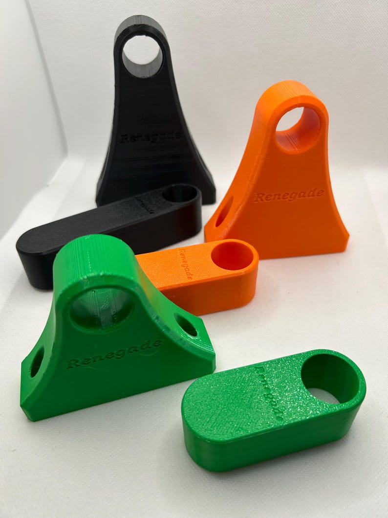 May include: A collection of 3D-printed Renegade phone stands in black, orange, and green. The stands have a distinctive design with a circular opening at the top and the word "Renegade" printed on the front.