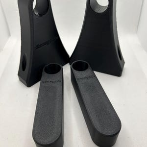 May include: Four black 3D-printed objects. Two are tall with a circular opening at the top and a smaller hole on the side. Two are rectangular with rounded ends. The word "Renegade" is printed on the objects.