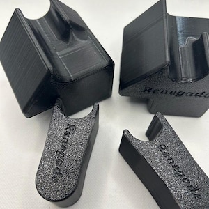 May include: Four black 3D-printed holders. Two are rectangular with a curved top, and two are smaller with the word "Renegade" printed on them. The holders are designed to hold an item.
