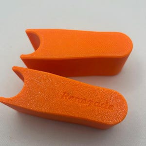 May include: Two bright orange, rectangular objects with a textured surface and a curved cutout on one end. The word "Renegade" is embossed on one of the objects. The objects are set against a white background.
